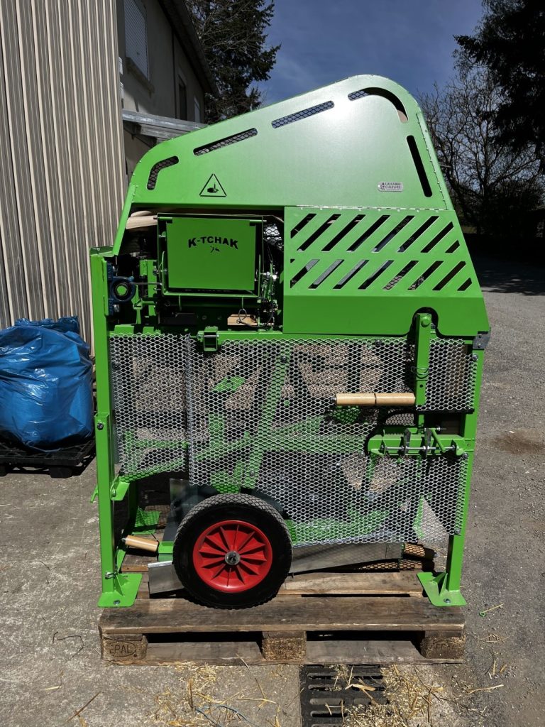 Vista lateral completa del triturador K-Tchak sobre césped, con manivela y ruedas de transporte Vista lateral completa del triturador K-Tchak sobre césped, con manivela y ruedas de transporte